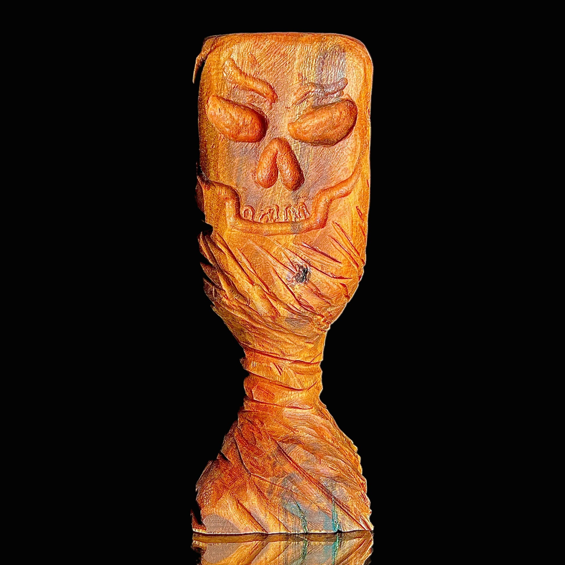 Wooden chalice with a carved skull on a black background.