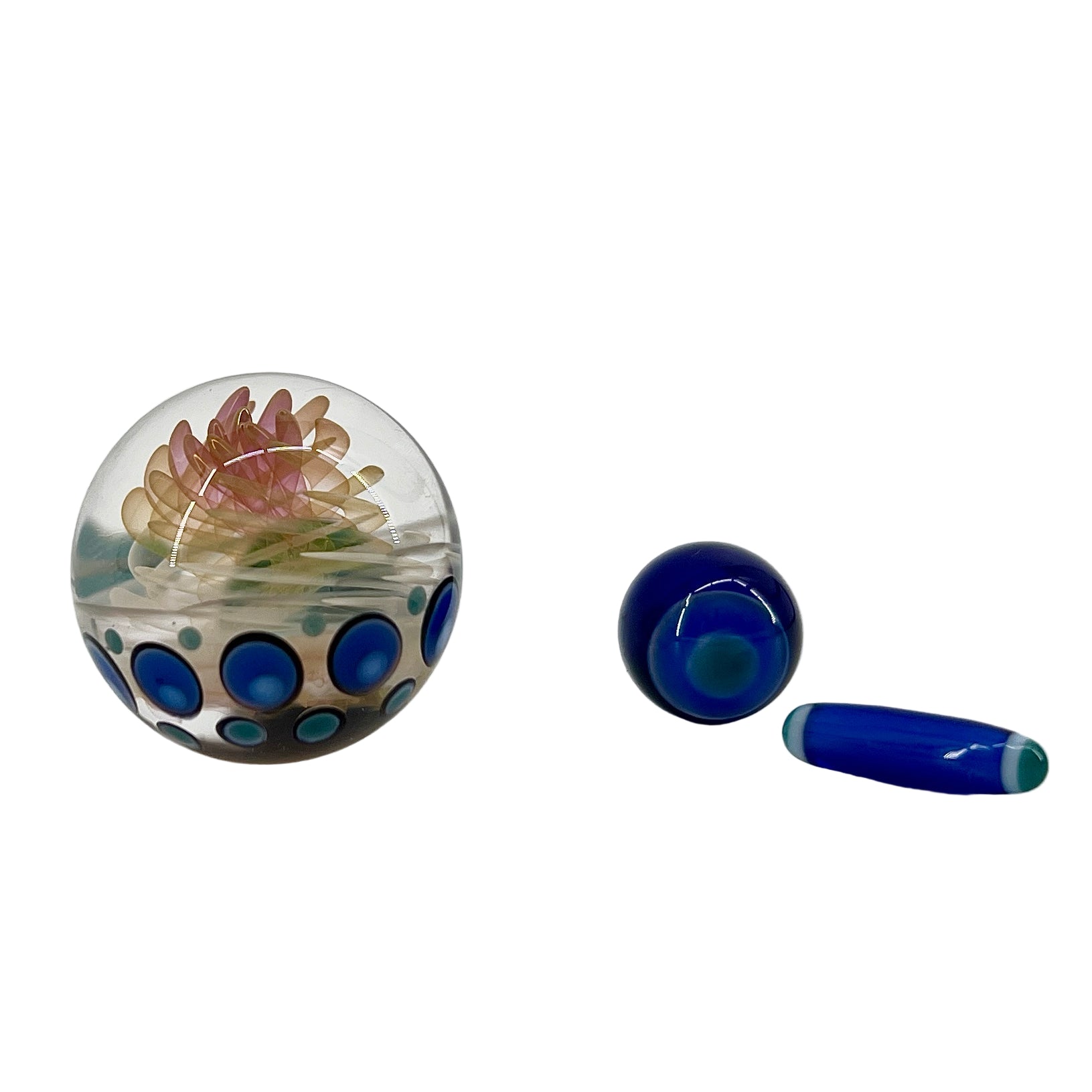 Glass paperweight with floral design and a blue cylindrical object on a white background