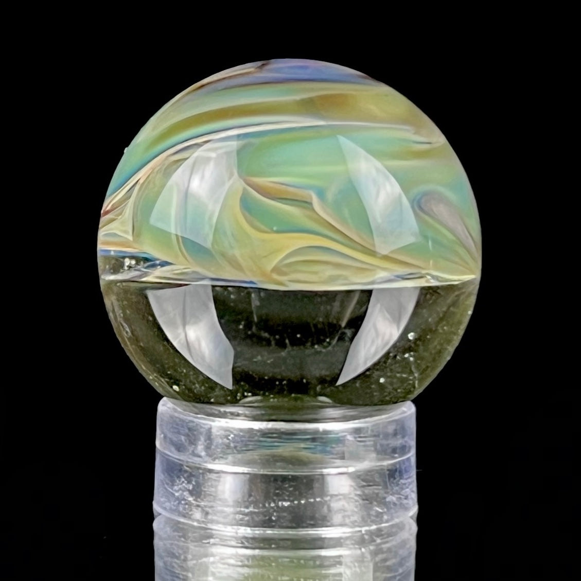 A multicolored glass marble with earth tones, placed on a glass stand.