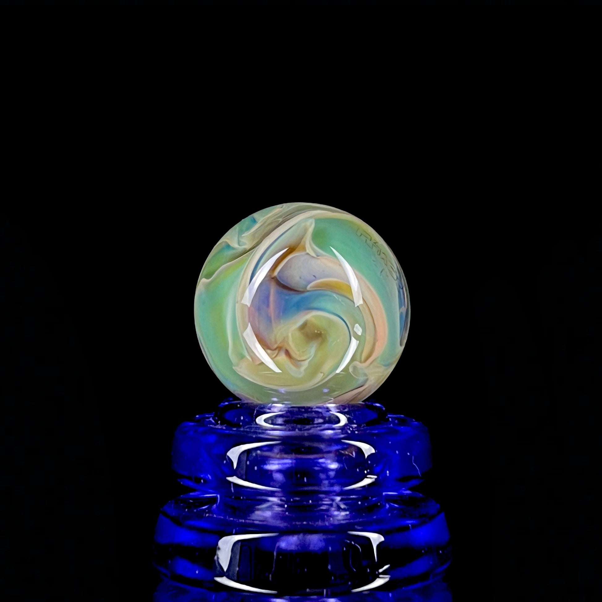 A multicolored glass marble with earth tones, placed on a blue stand, against a black background.