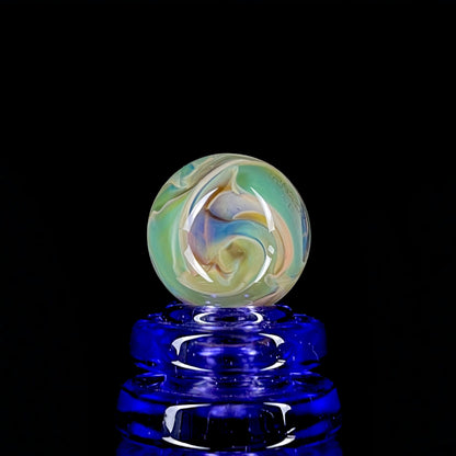 A multicolored glass marble with earth tones, placed on a blue stand, against a black background.