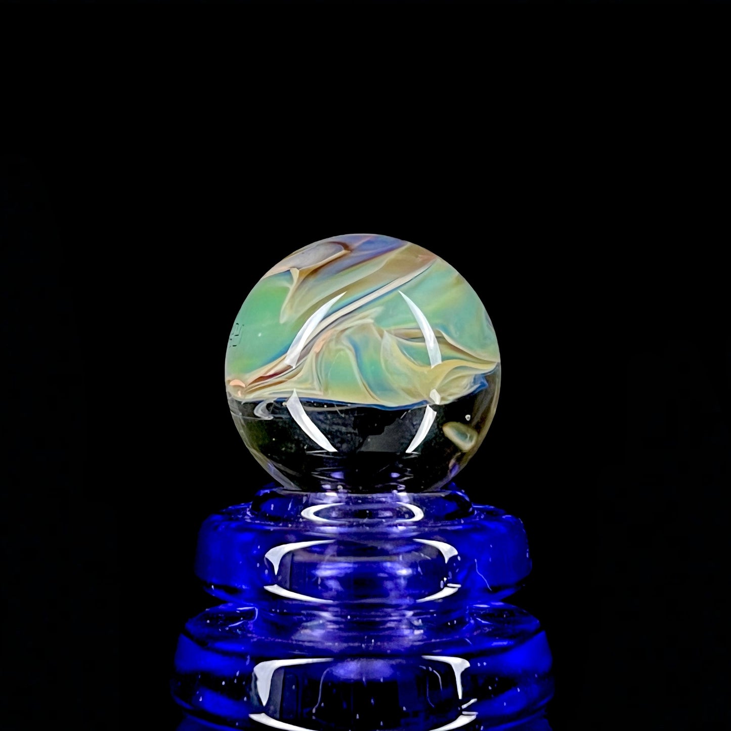 A multicolored glass marble with earth tones, placed on a blue glass stand.