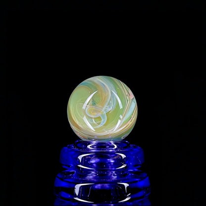 A multicolored glass marble with earth tones, placed on a blue glass stand.