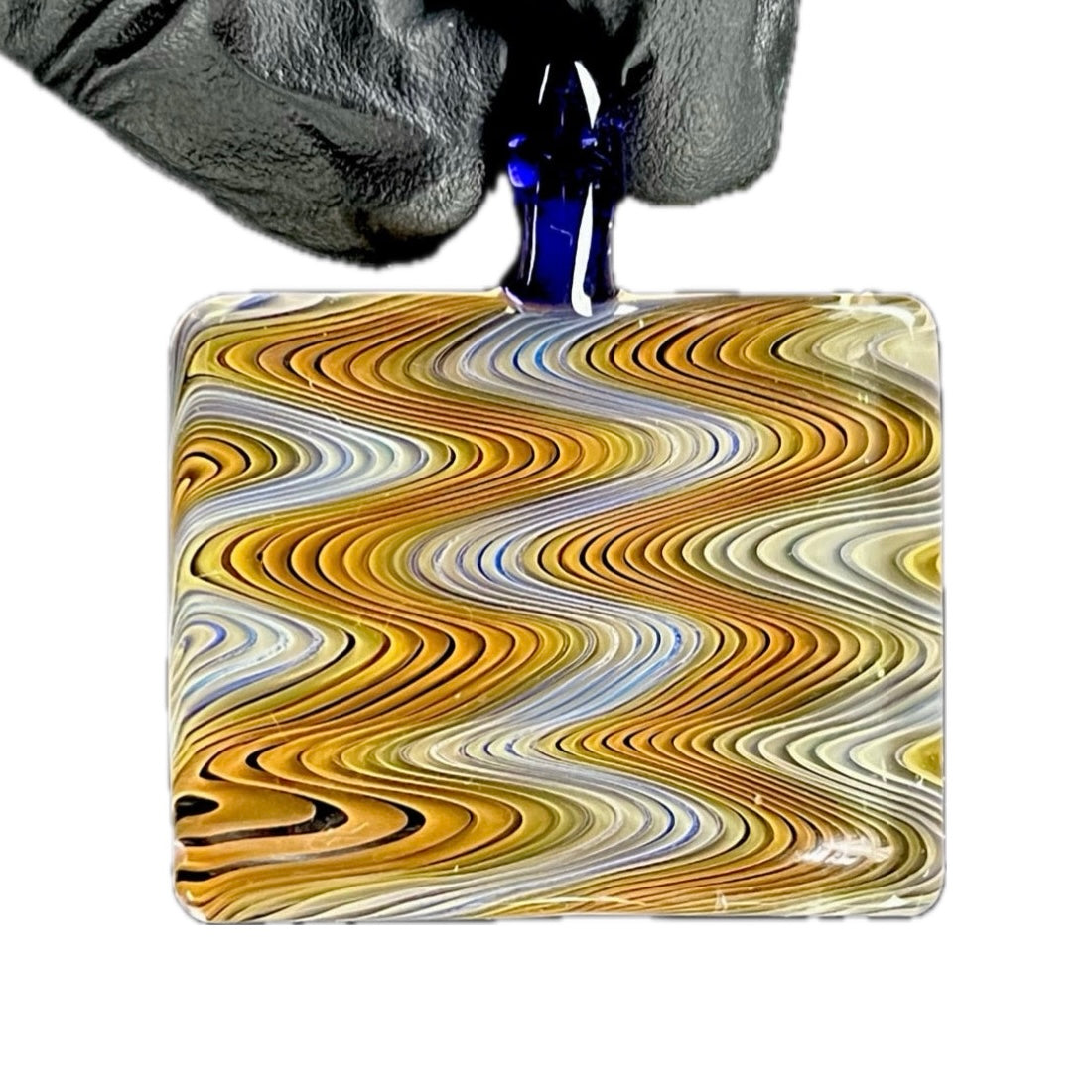 A hand holding a rectangular glass pendant with a swirling pattern of yellow, brown, and white colors.