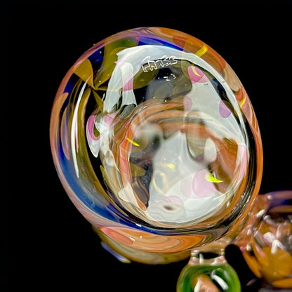 A close up of a multicolored glass hammer-style pipe with intricate patterns and a round bowl.