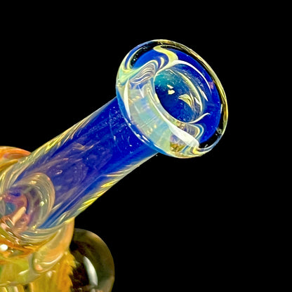 A colorful glass hammer-shaped piece with blue, gold, and silver fume patterns.
