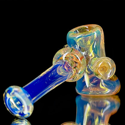 A colorful glass hammer-shaped piece with blue, gold, and silver fume patterns.