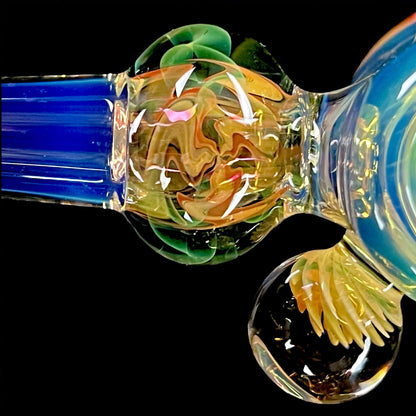 A colorful glass hammer-shaped piece with blue, gold, and silver fume patterns.