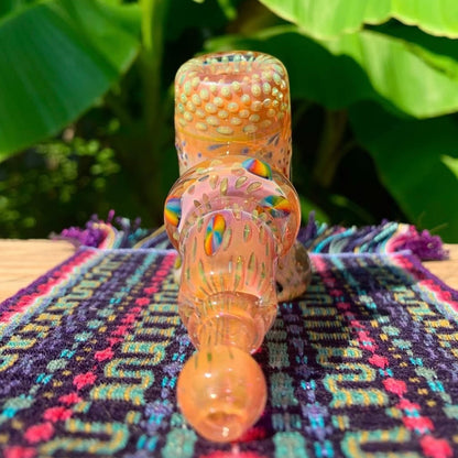 Decorative glass pipe with colorful patterns on a patterned surface with green leaves in the background.
