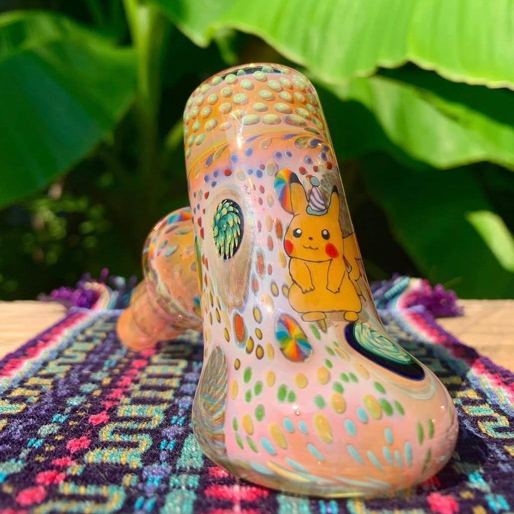 Colorful glass pipe with cartoon character design on a patterned surface with green leaves in the background.