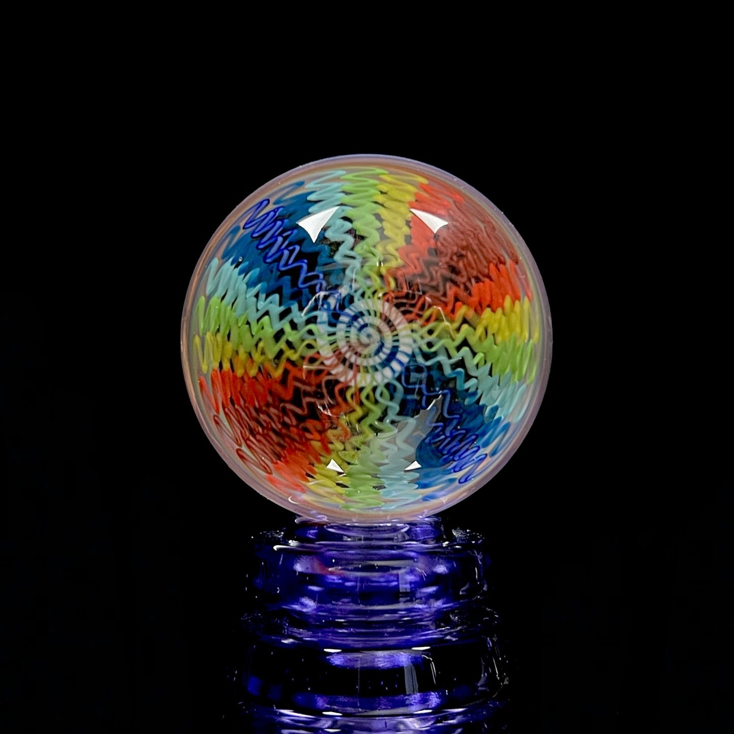 A multicolored spiral pattern marble with a predominantly black center and radiating swirls of blue, red, and green.