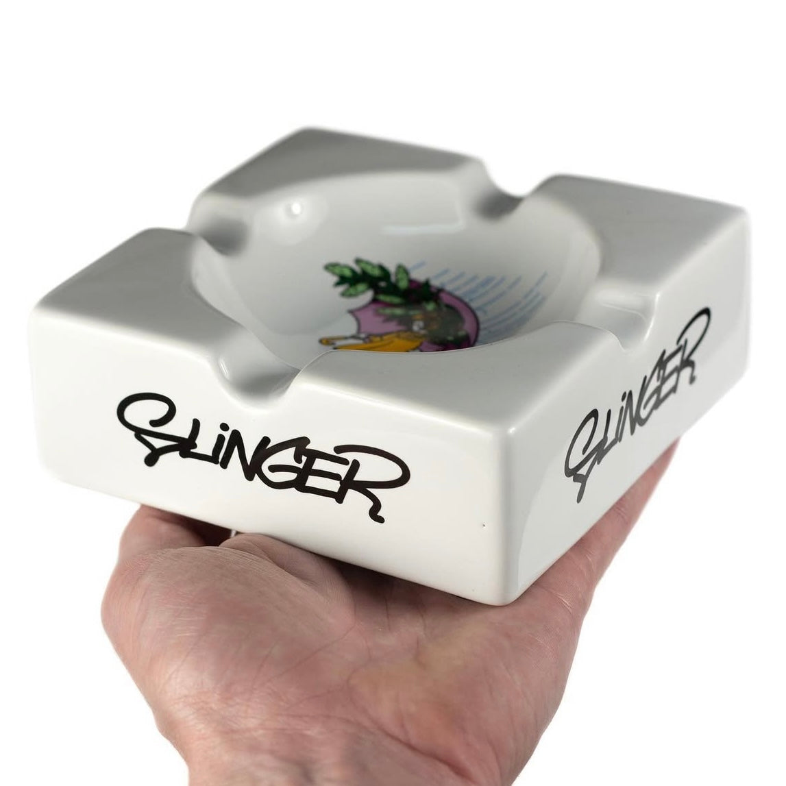 White ceramic ashtray with 'Slinger' branding held by a hand on a white background.