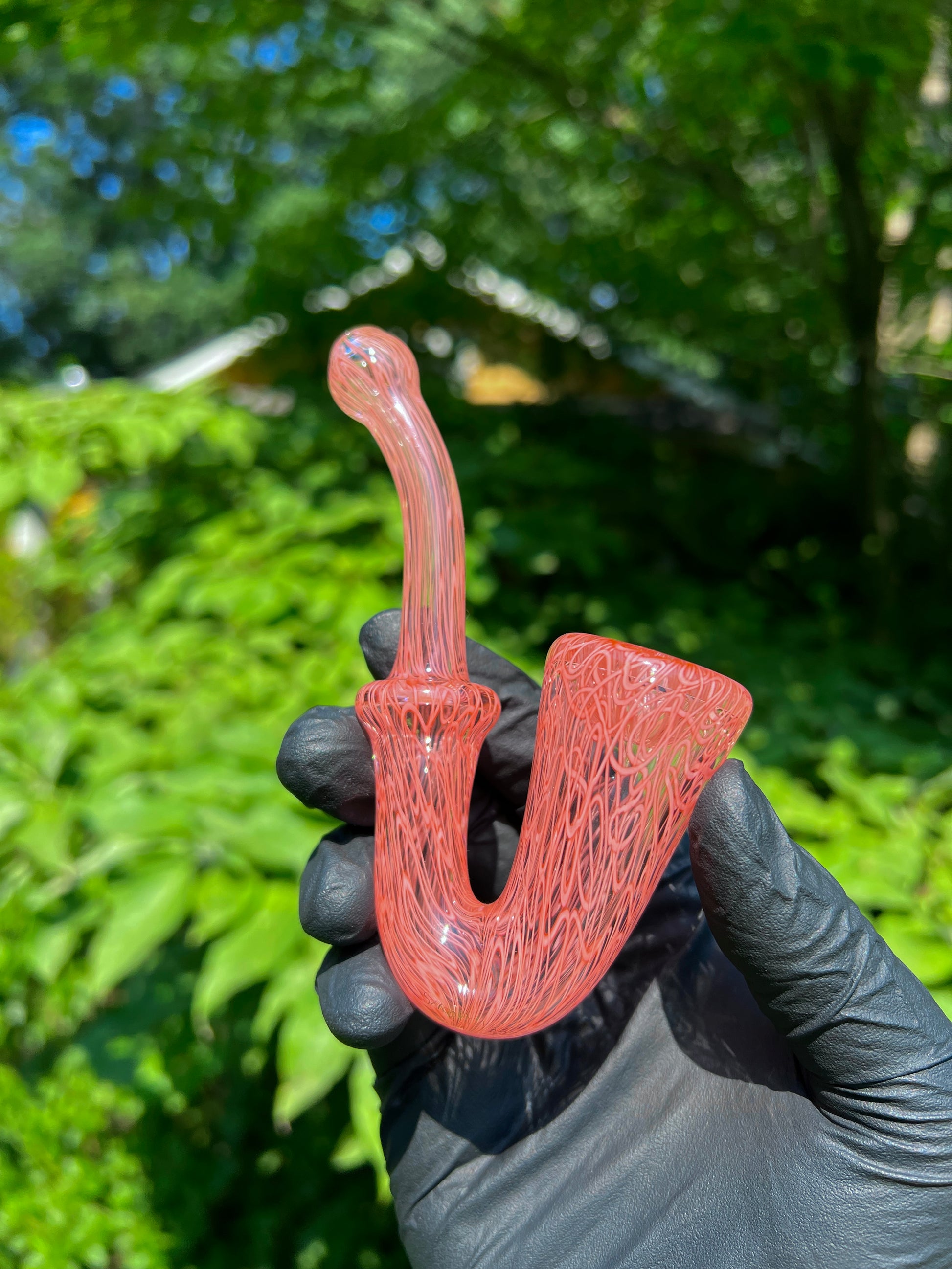 A red glass pipe with a intricate pattern, featuring a bowl and a curved stem.
