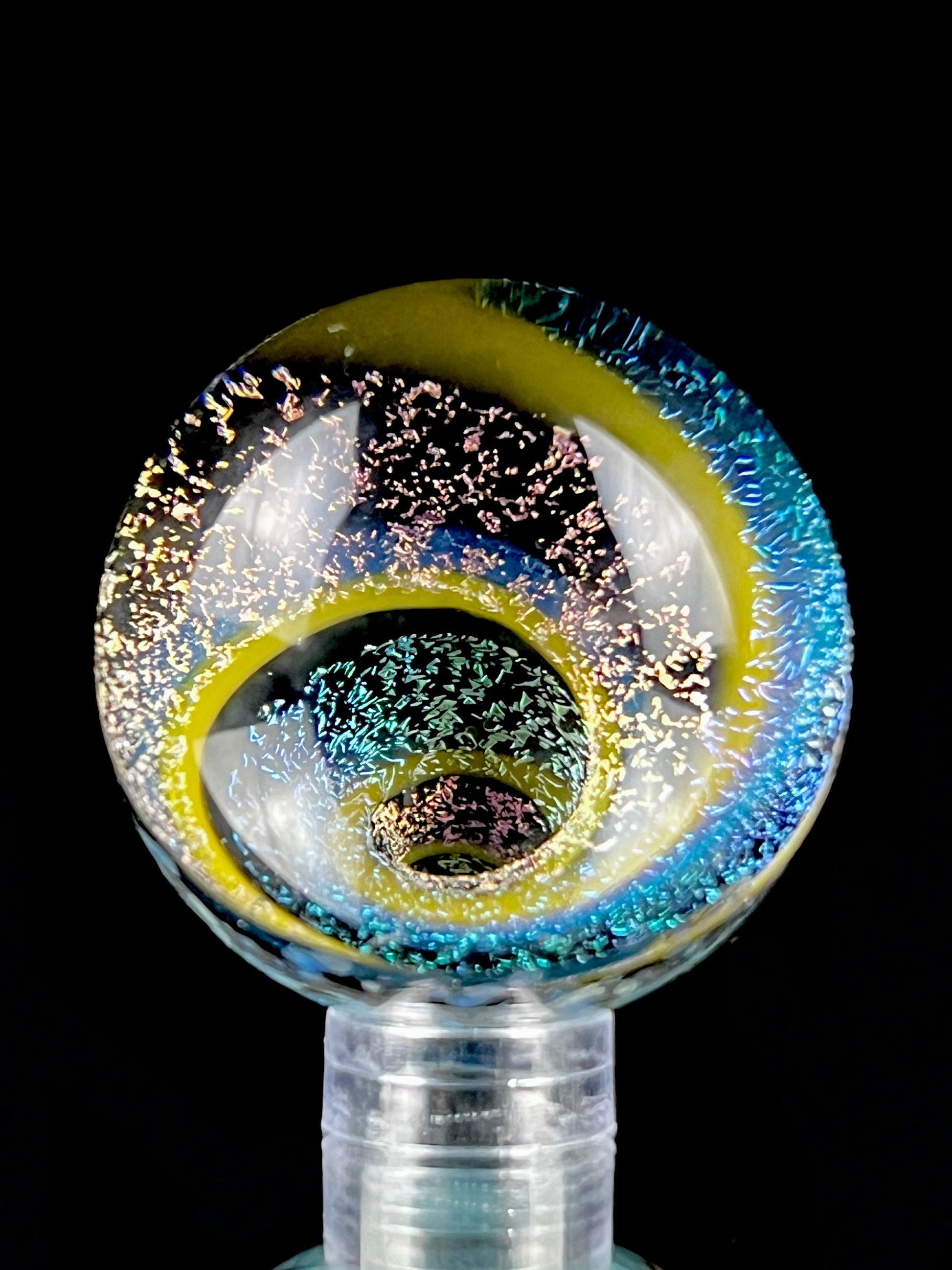 A multicolored glass marble with a visible swirling pattern, predominantly in blue and yellow hues, against a black background.