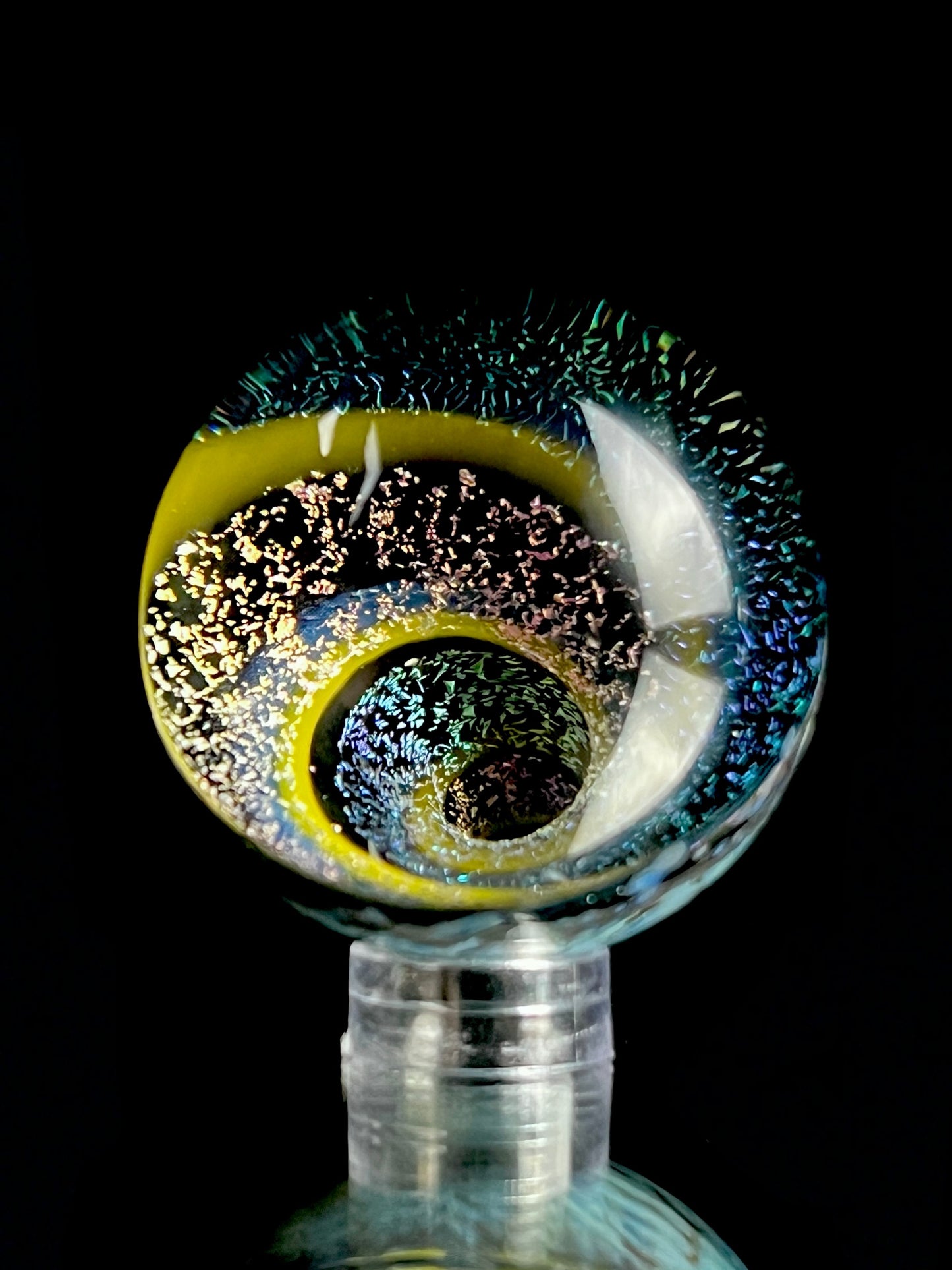 A multicolored glass marble with a visible swirling pattern, predominantly in blue and yellow hues, against a black background.
