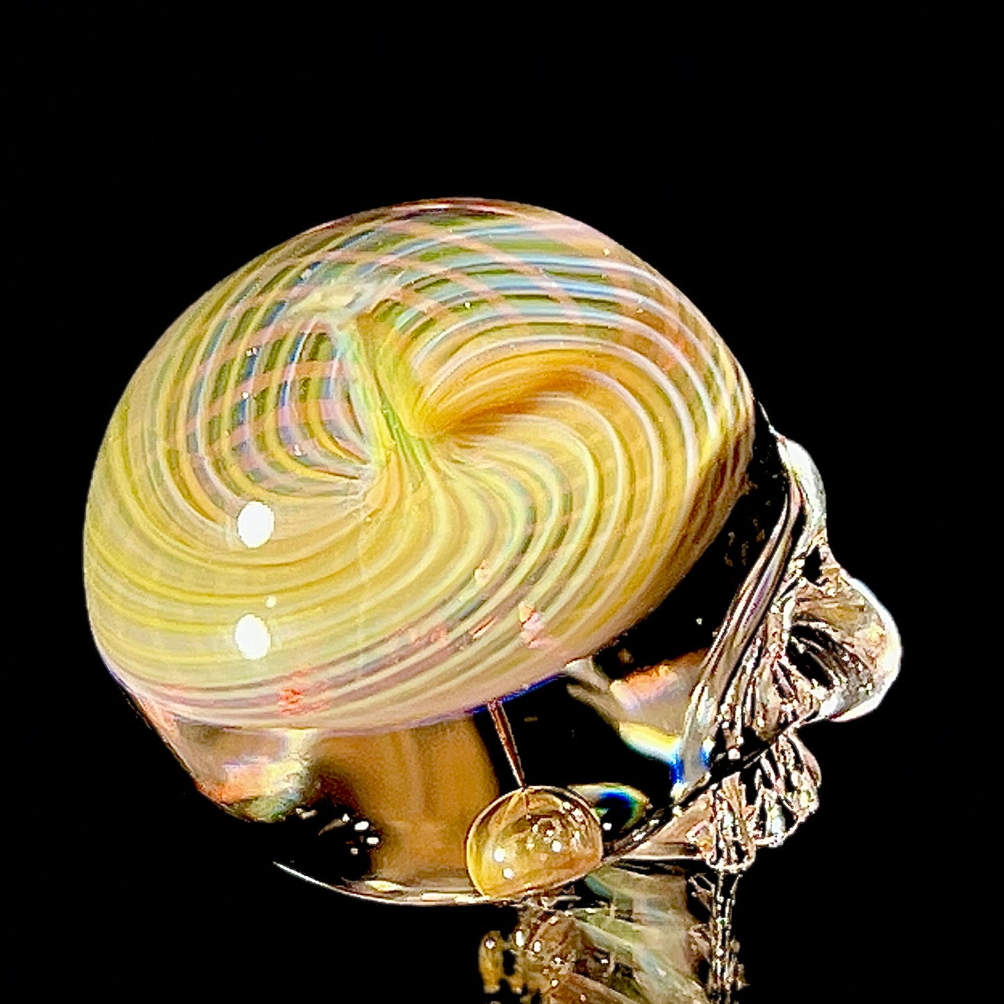 Glass sculpture of a skull with a multicolored swirl on a black background