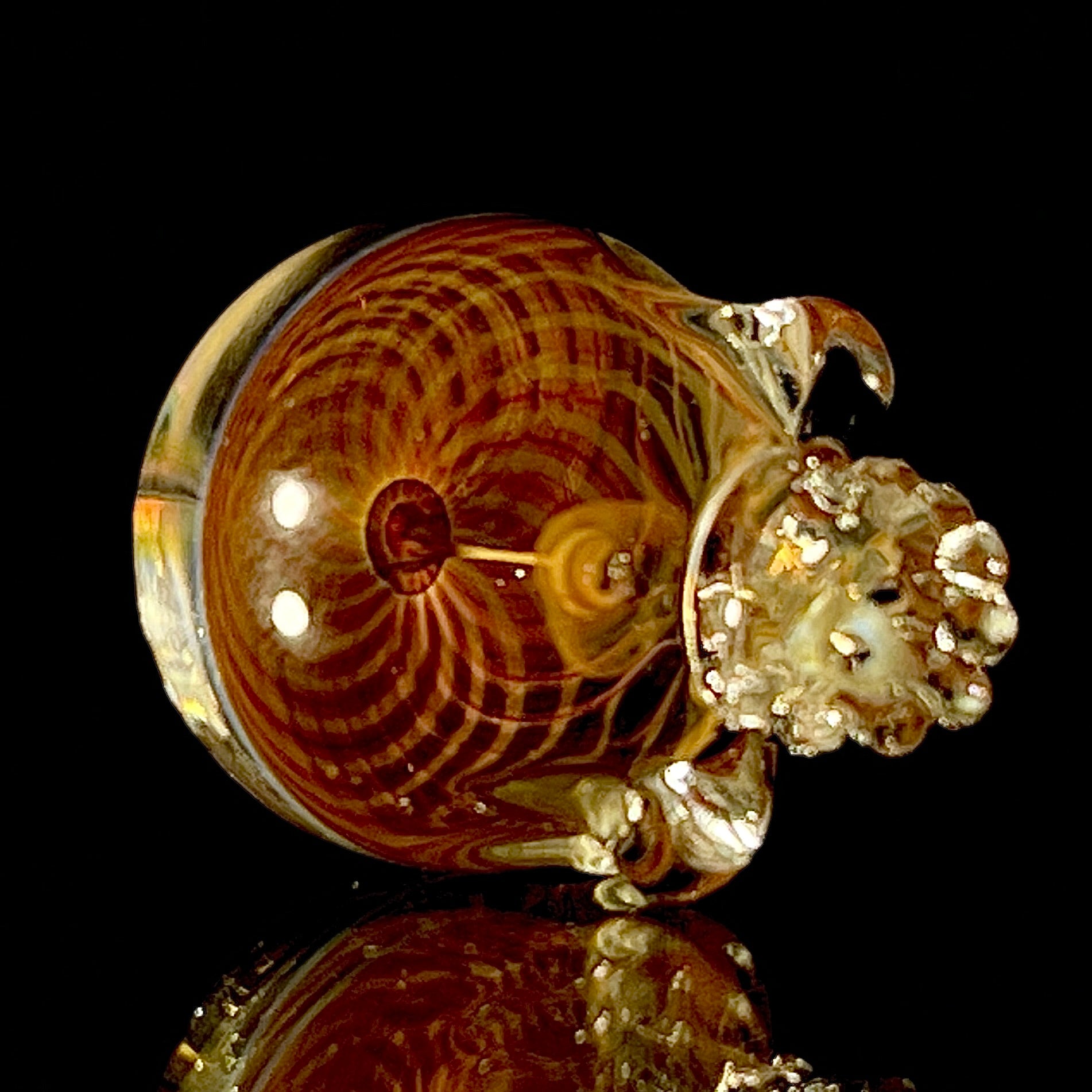 Glass sculpture of a skull with a brown and gold spiral on a black background