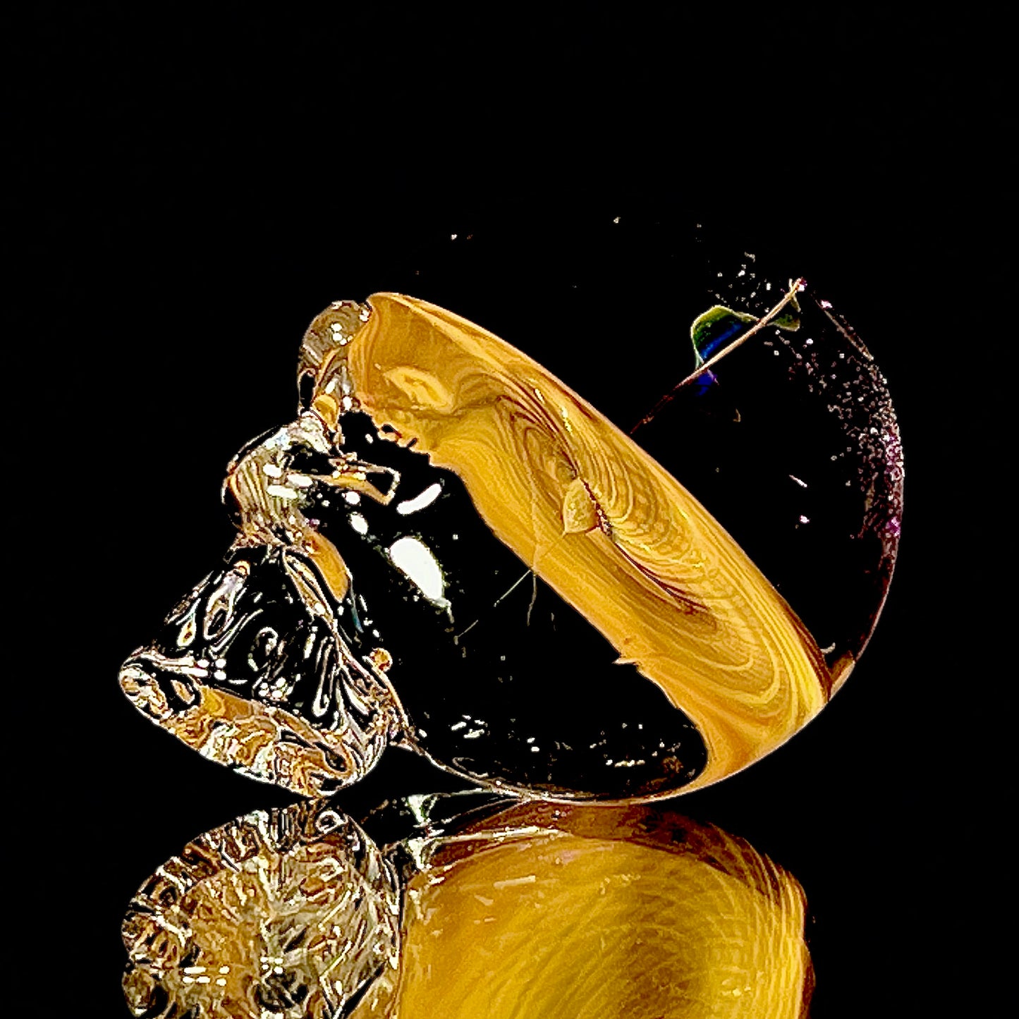 Gold fumed glass skull with intricate design on a reflective surface.