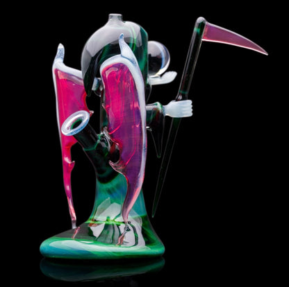 A custom glass piece by Joachim Dallant featuring a winged reaper figure with a colorful backdrop, incorporating a Fumicello orb and a removable scythe dabber.