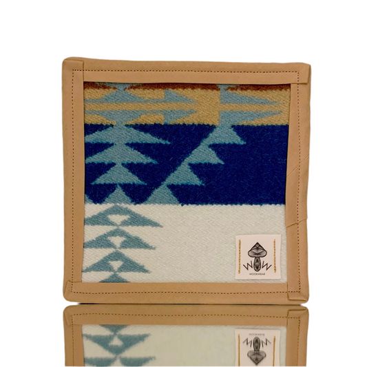 A square-shaped Pendleton mat with geometric patterns in blue, beige, and other colors, framed with a tan border.