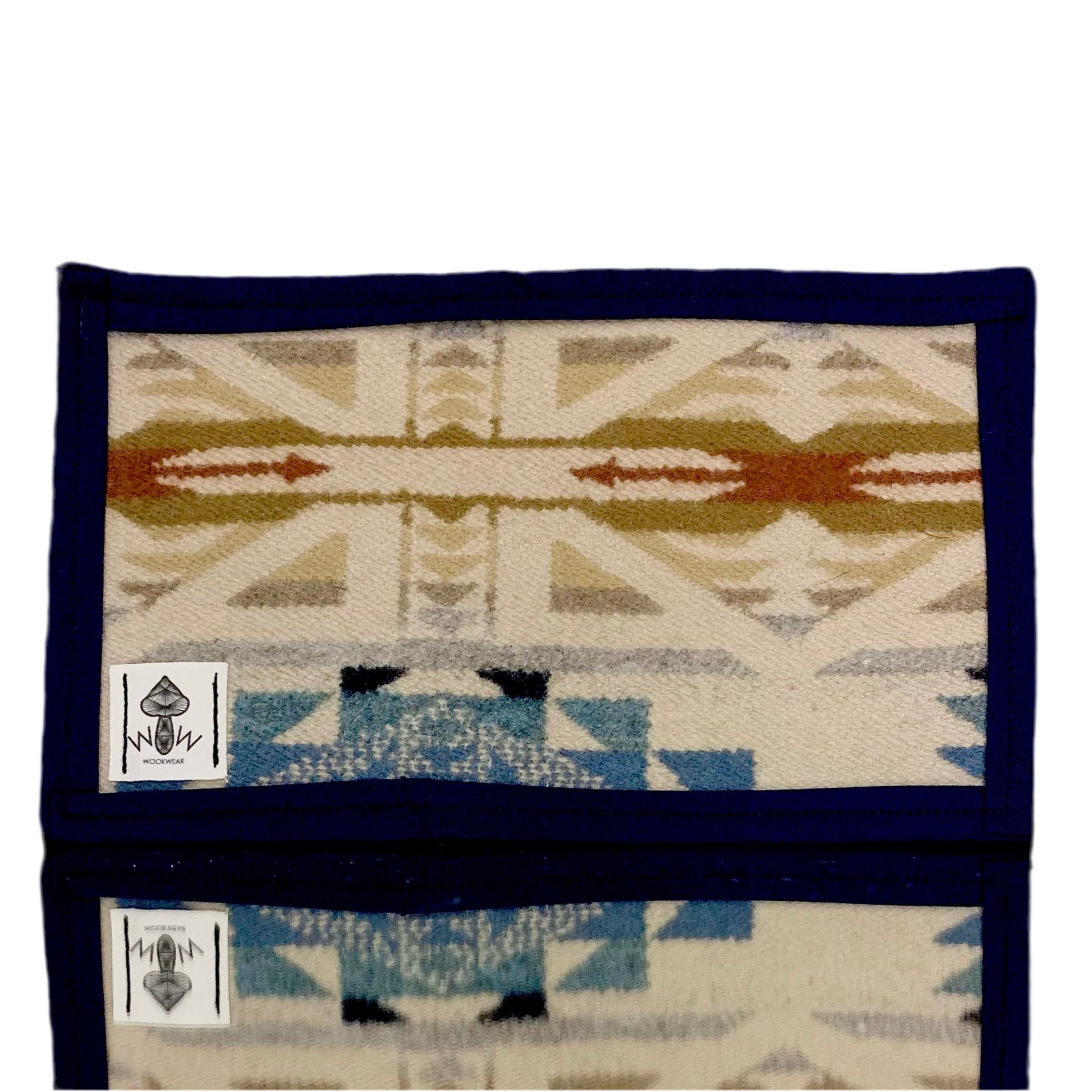 A Pendleton mat featuring a geometric pattern with a mix of blue, beige, and red colors, with a label showing the brand name 'Wook Wear'.