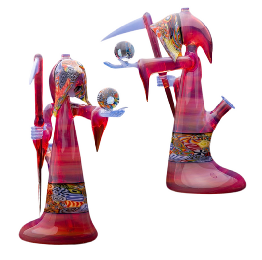 A colorful glass pipe shaped like a reaper with a scythe, featuring abstract designs and a removable dabber.