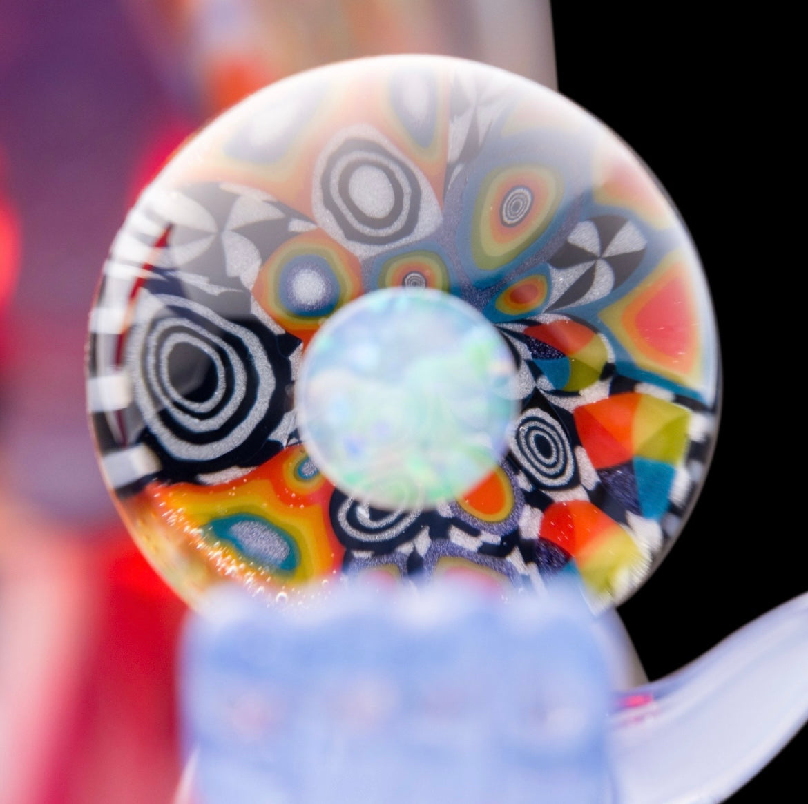 A colorful glass pipe shaped like a reaper with a scythe, featuring abstract designs and a removable dabber.