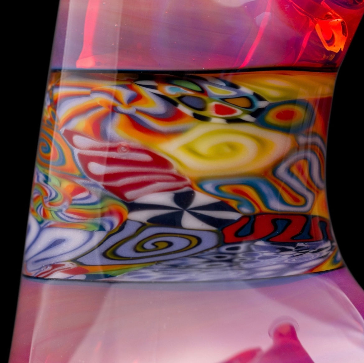 A colorful glass pipe shaped like a reaper with a scythe, featuring abstract designs and a removable dabber.