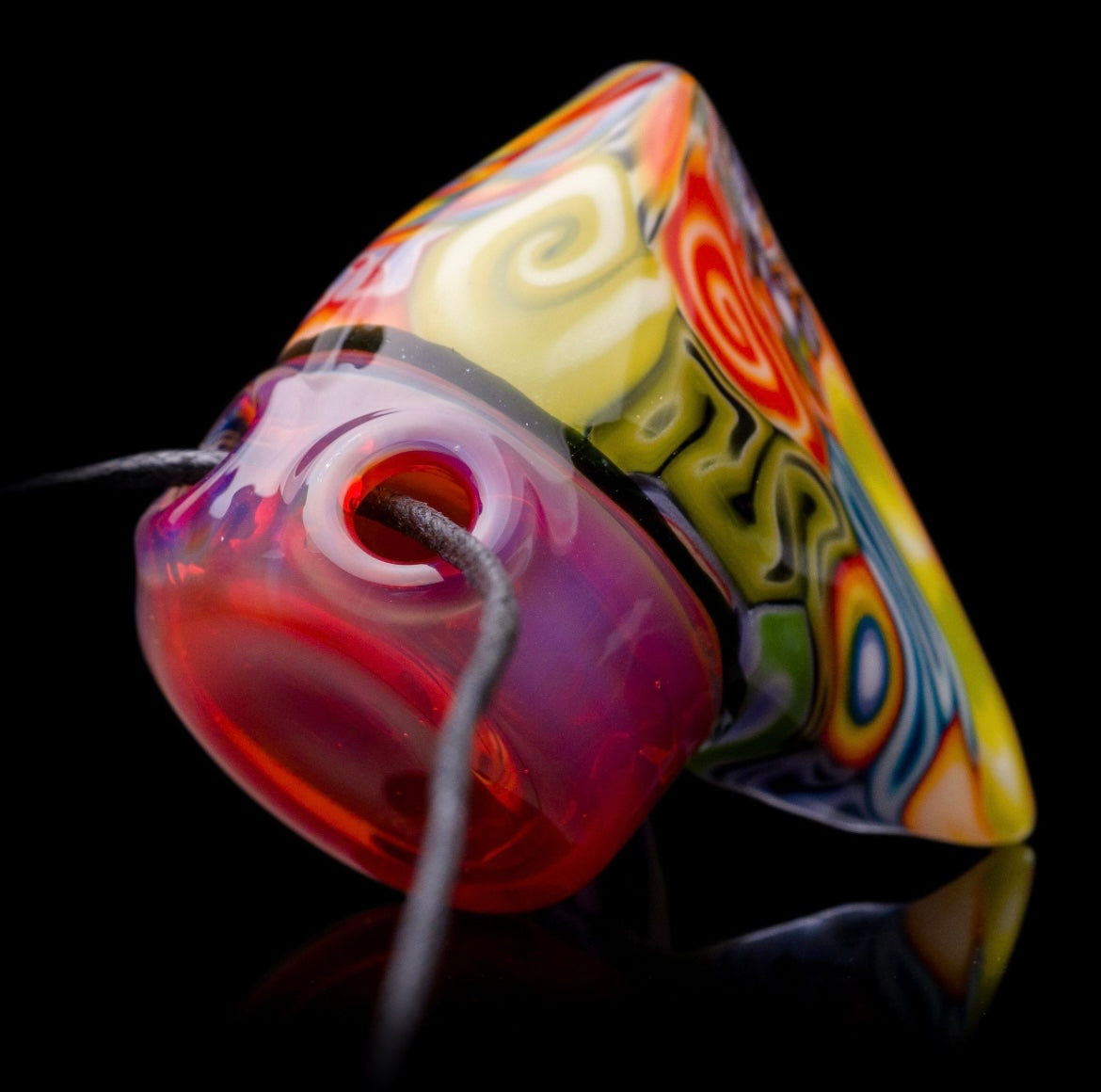 A colorful glass pipe shaped like a reaper with a scythe, featuring abstract designs and a removable dabber.