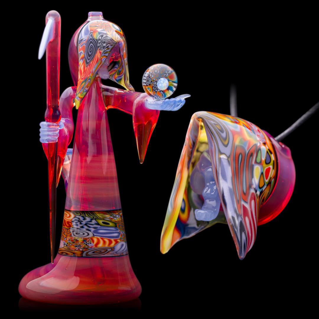 A colorful glass pipe shaped like a reaper with a scythe, featuring abstract designs and a removable dabber.