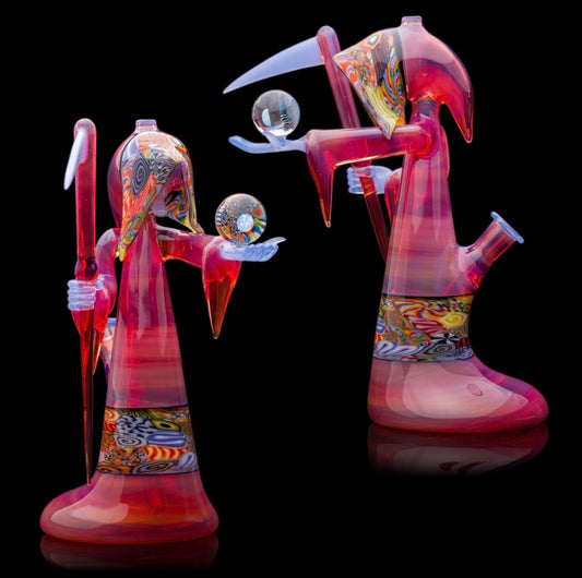 A colorful glass pipe shaped like a reaper with a scythe, featuring abstract designs and a removable dabber.