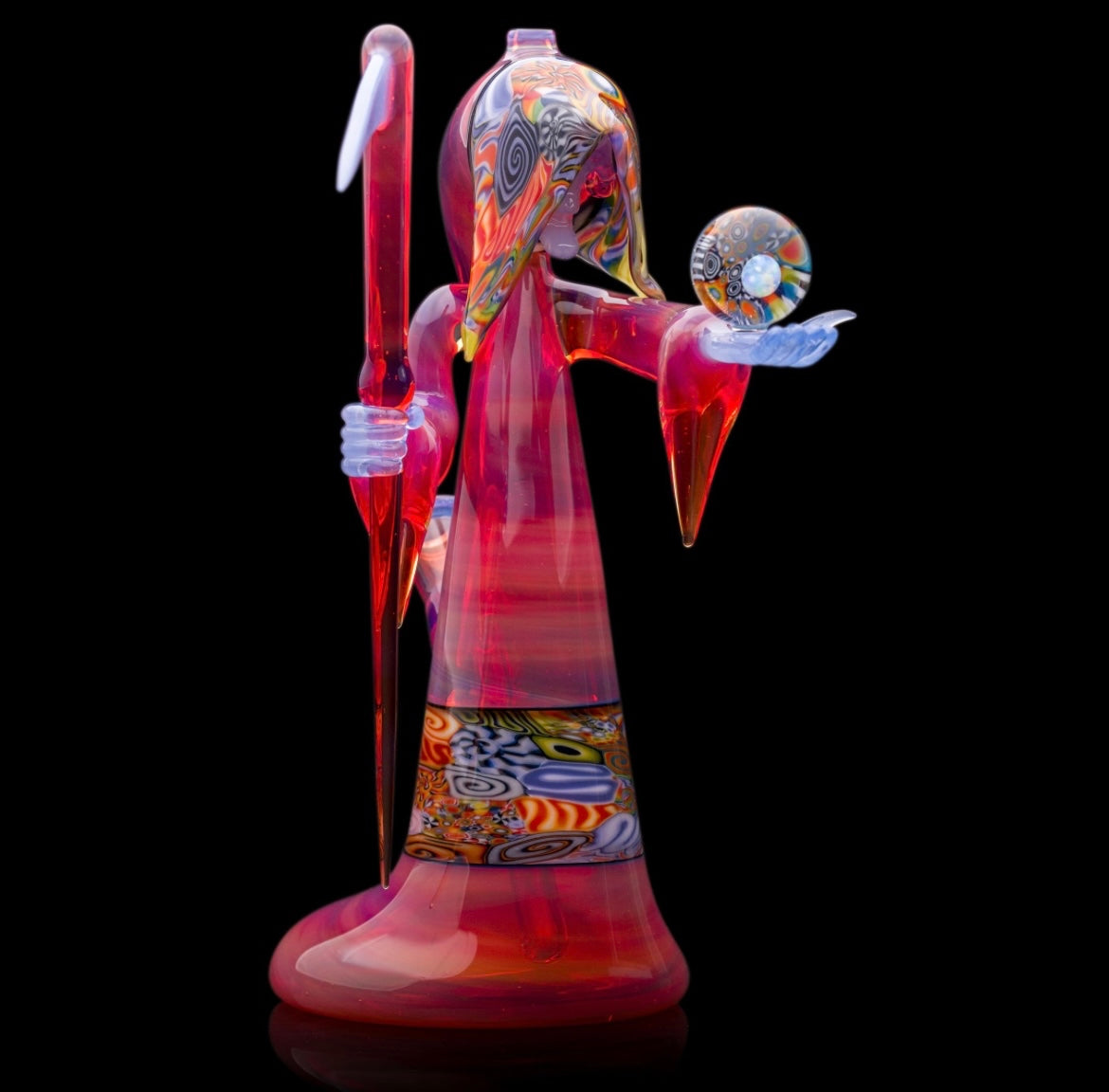 A colorful glass pipe shaped like a reaper with a scythe, featuring abstract designs and a removable dabber.